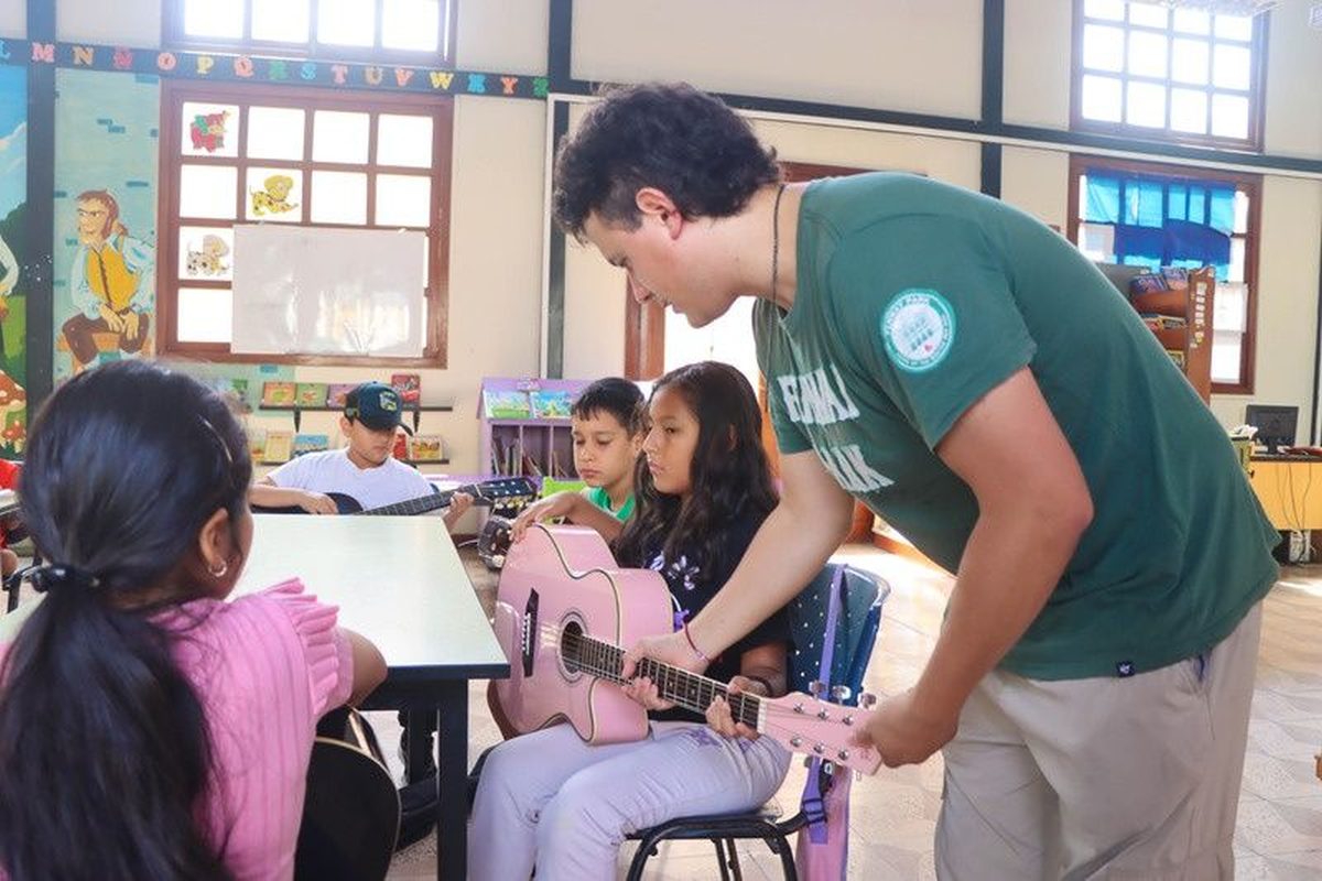 El docente corrige la postura de una alumna con su guitarra